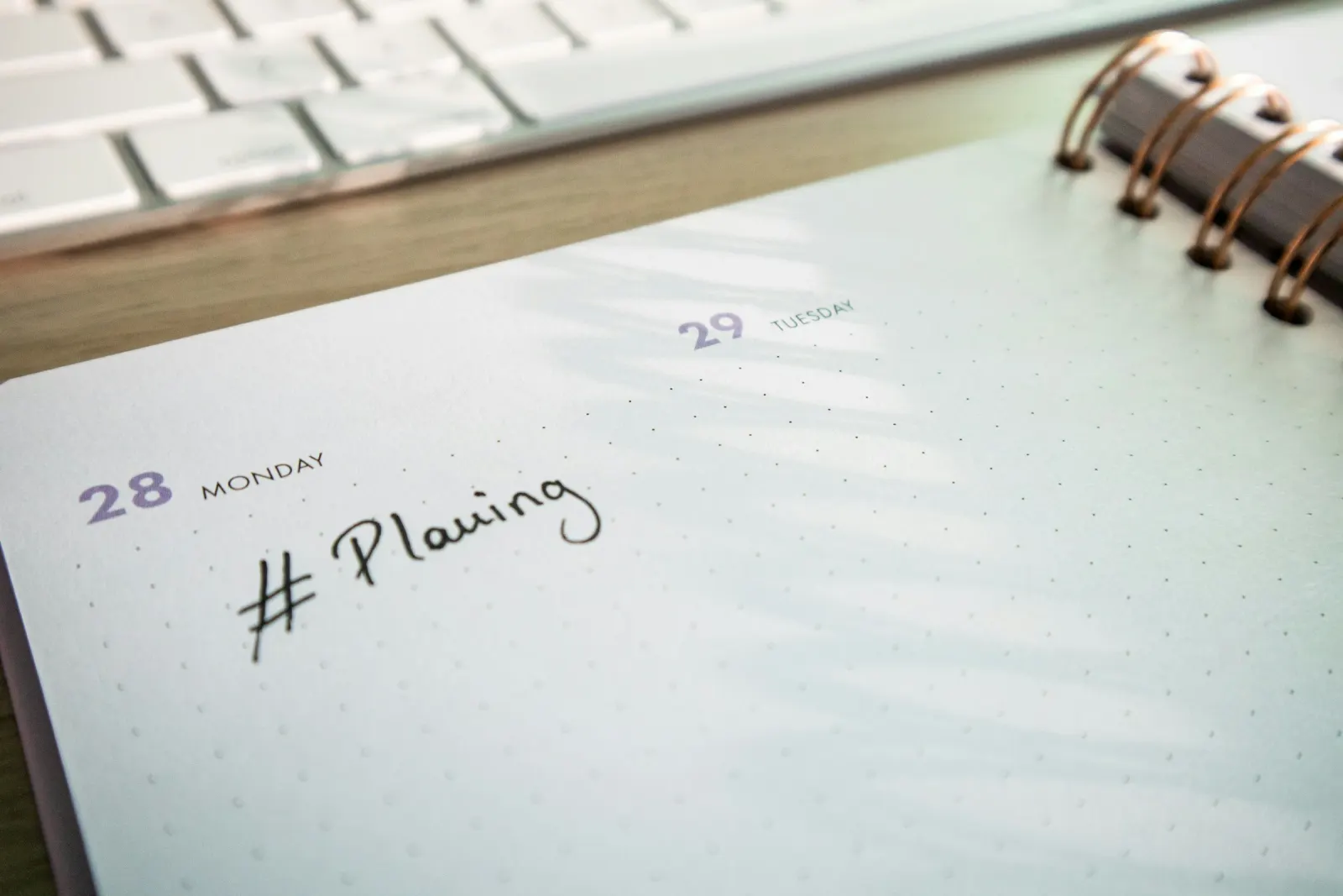 An open weekly planner on a desk with a keyboard behind it