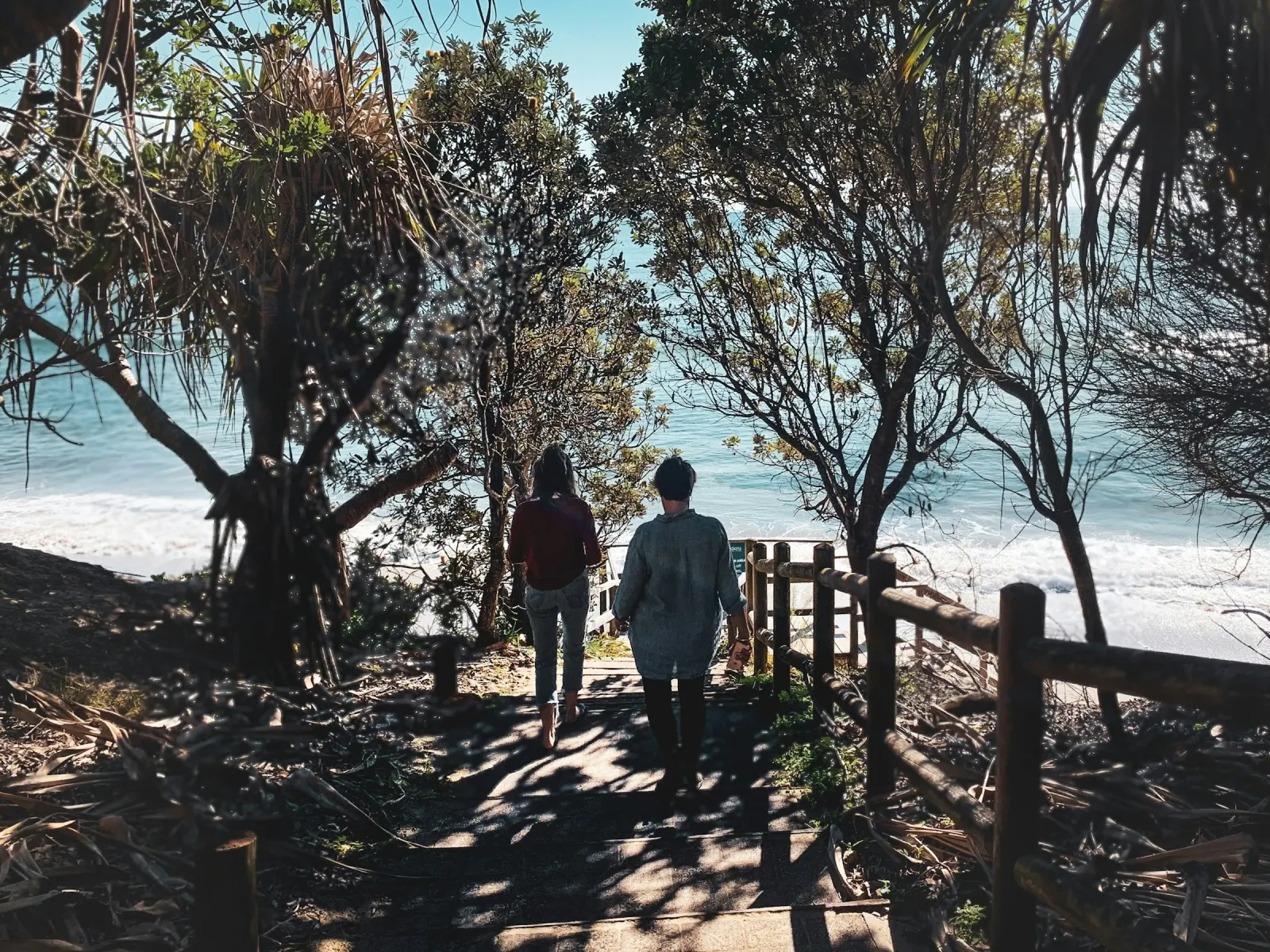 A man and a woman walking down a shaded track through coastal trees towards the beach at Byron Bay, New South Wales
