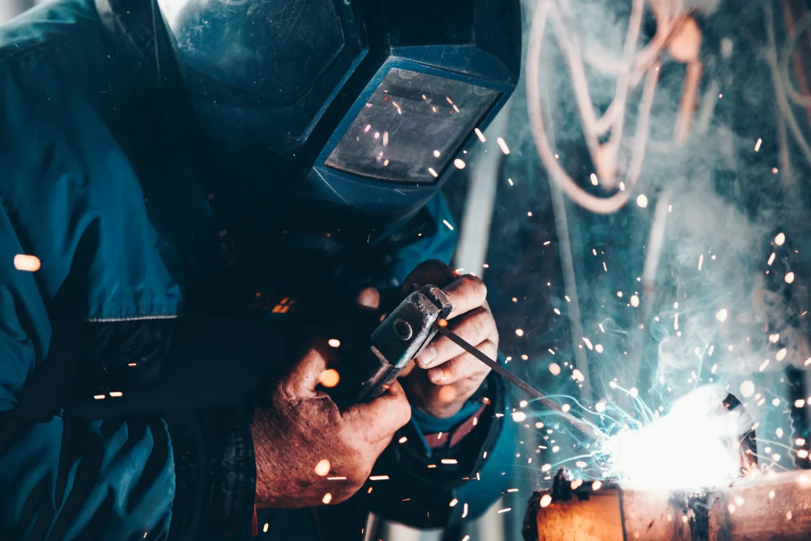A welder in a protective helmet joining steel as sparks fly in a workshop in Hay, New South Wales