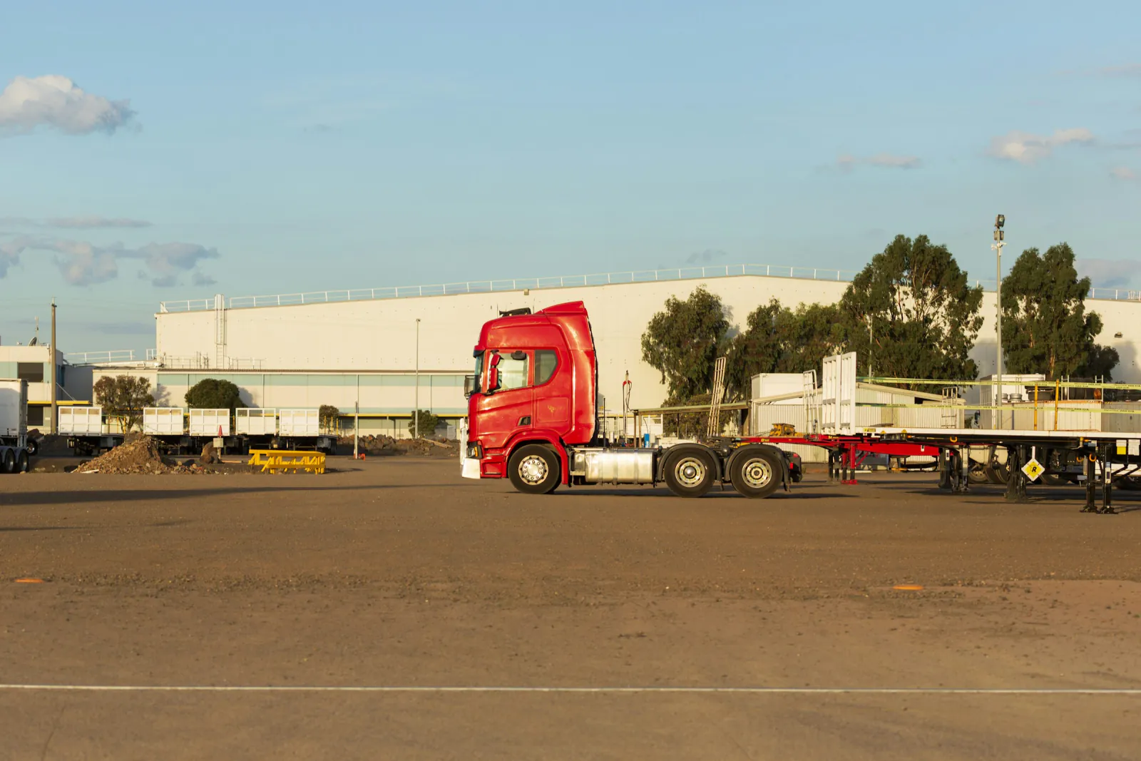 A large warehouse beside a gravel yard with a red prime mover parked in front, Altona, Victoria